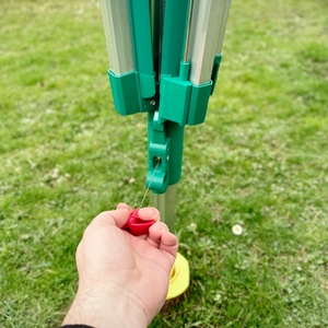 Eine Hand zieht an der roten Aufziehkordel der Leifheit Linomatic 600 Deluxe auf einer Rasenfläche.