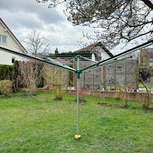 Die Leifheit Linomatic 600 Deluxe steht geöffnet im Garten mit aufgespannten Leinenarmen.
