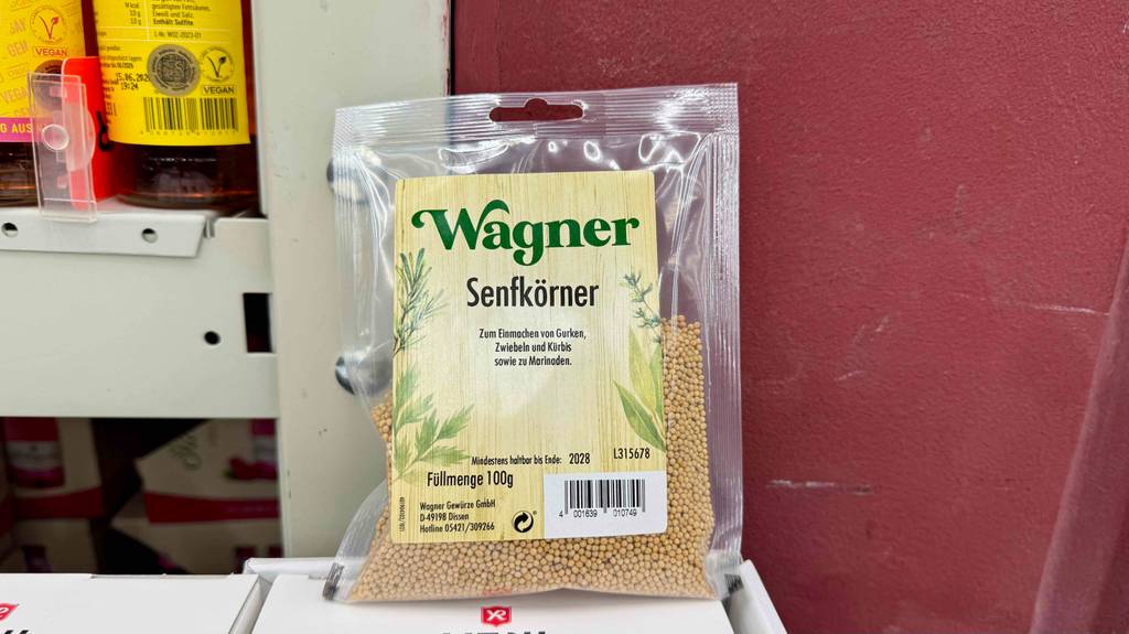 Eine Packung getestete Senfkörner steht vor einer roten Wand.