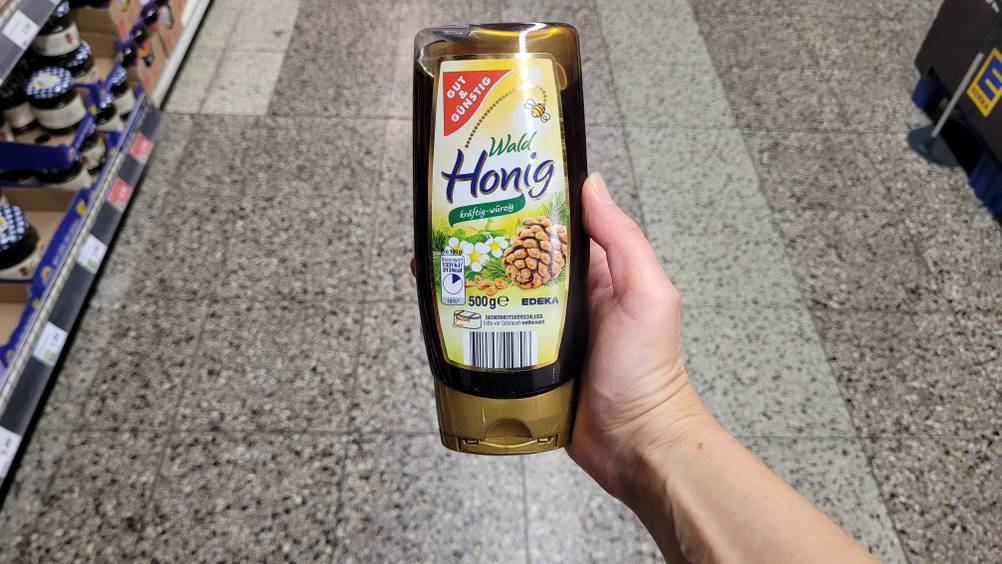 Eine Hand hält eine Flasche des getesteten Waldhonigs in einem Verkaufsladen.