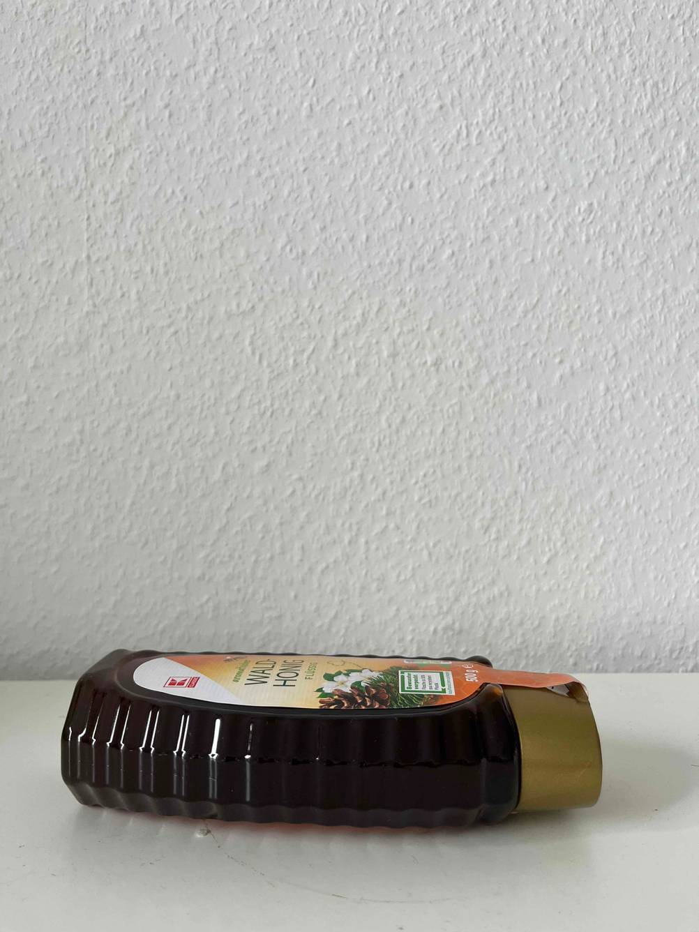 Getestet: Eine Flasche Waldhonig liegend von der Seite vor einer hellen Wand.
