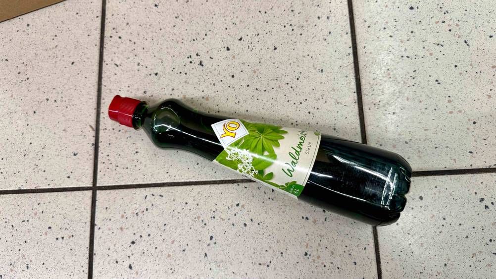 Auf einem Fließenboden liegt horizontal eine Flasche des Waldmeistersirups im Test.