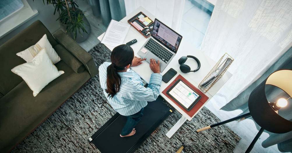 Laufband mit Steigung im Test: Ein Mann mit langen Haaren geht im Home Office auf einem Walking Pad, während er arbeitet. Ansicht von oben.