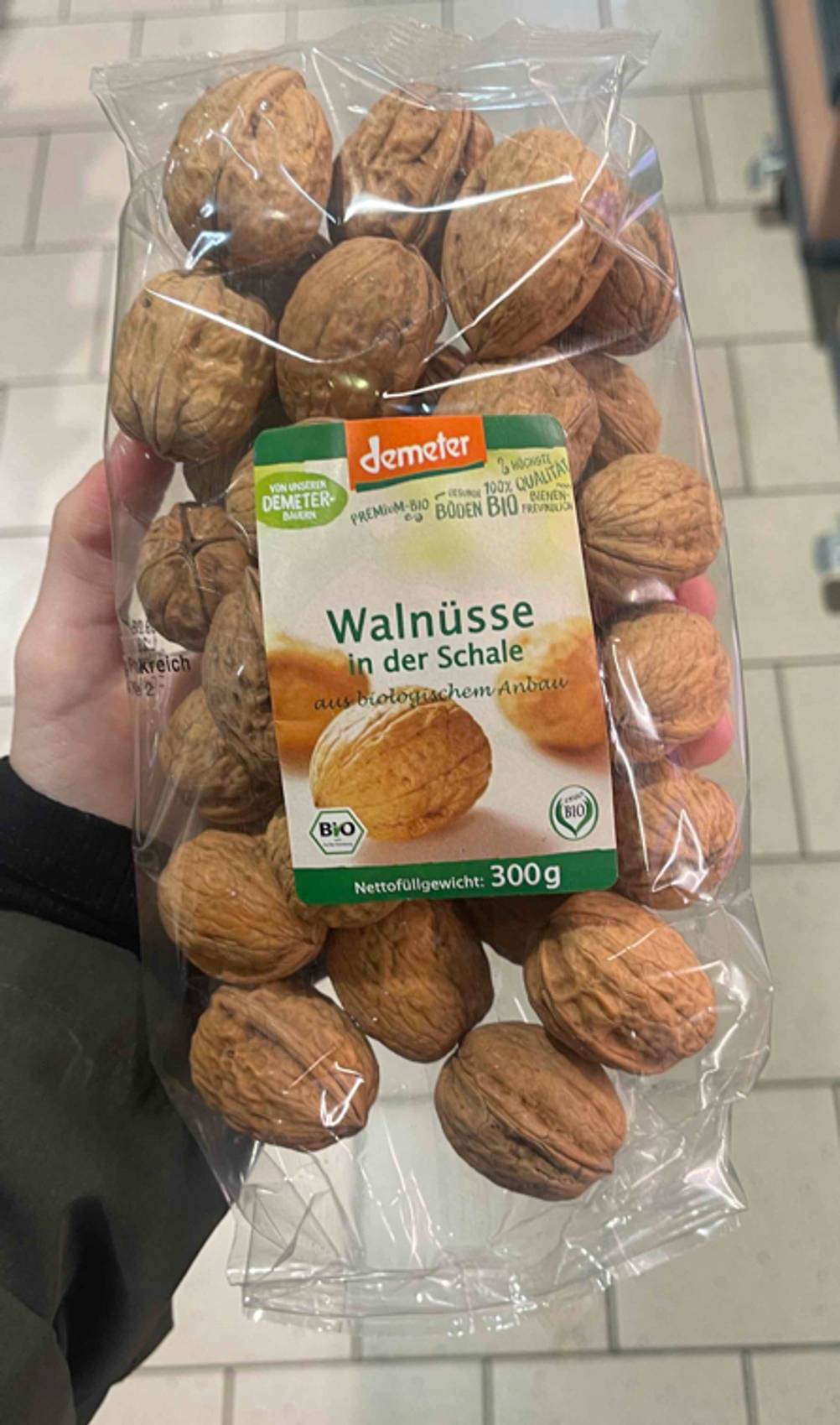 Getestet: Die Walnüsse mit Schale befinden sich in einer transparenten 300-g-Tüte der Marke Demeter, die von einer Hand gehalten wird.
