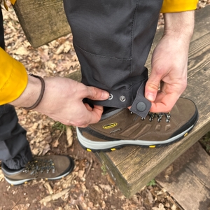 Eine Hand stellt das Beinende der RevolutionRace Herren GPX Pro Hose mit Druckknöpfen enger. Die Anpassung sorgt für besseren Sitz über Schuhen.