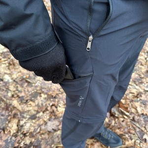 Eine Hand steckt ein Smartphone in die seitliche Reißverschlusstasche der Vaude Herren Farley Stretch T-Zip Hose III. Die Tasche bietet schnellen Zugriff auf wichtige Gegenstände.