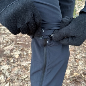 Eine Person öffnet mit schwarzen Handschuhen den T-Zip Reißverschluss der Vaude Herren Farley Stretch T-Zip Hose III. Der Zipper ermöglicht das einfache Abnehmen des Hosenbeins.