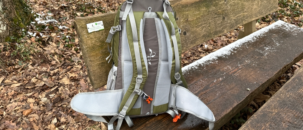 Die Rückseite des Mountaintop-TX5832lanpeicheng-Wanderrucksacks mit gepolstertem Rückensystem und verstellbaren Gurten. Der Rucksack steht auf einer Bank im Wald.