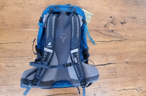 Die Rückseite eines blauen deuter Wanderrucksacks liegt flach auf einem Holzboden. Das Rückensystem und die gepolsterten Gurte sind gut sichtbar.
