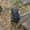 Der Vaude-14394-Wanderrucksack steht allein auf einer Bank im Wald. Das Modell ist geschlossen und vollständig bepackt.