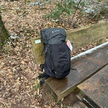 Der Vaude-14394-Wanderrucksack steht allein auf einer Bank im Wald. Das Modell ist geschlossen und vollständig bepackt.