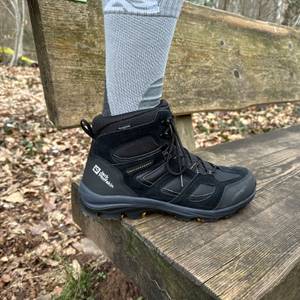 Seitenansicht des getragenen Jack Wolfskin Vojo 3 Texapore Mid M auf einer Holzbank. Der halbhohe Schaft und die Markenlogos sind gut sichtbar.