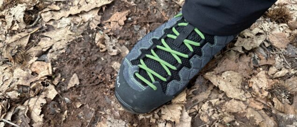 Der Salewa Ms Alp Trainer Mid getragen auf einem Waldboden mit Laub. Der Schuh ist vollständig geschnürt und im Einsatz zu sehen.