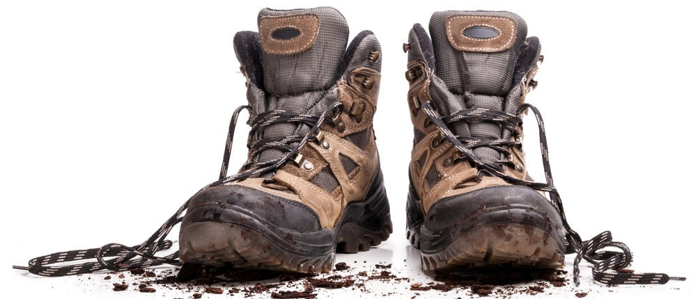Zwei stark verschmutzte Wanderschuhe mit offenen Schnürsenkeln stehen nebeneinander. Der Boden unter den Schuhen ist mit Erde bedeckt.