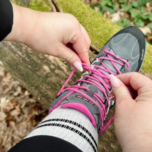 Zwei Hände ziehen einen Knoten in die Schnürsenkel des CMP-Rigel-Mid-Wanderschuhs. Der Schuh liegt auf einem Baumstamm.