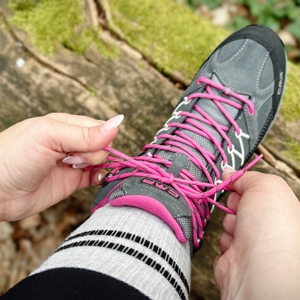 Ein gebundener Schleifenknoten der pinken Schnürung am CMP Rigel Mid, aufgenommen im Wald auf einem Baumstamm.