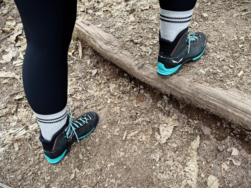 Zwei Salewa-MTN-Trainer-Mid-GTX-Wanderschuhe auf trockenem Waldboden, getragen von einer Person im Test.