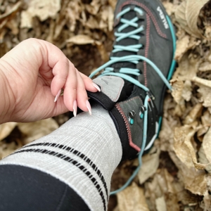 Wanderin mit Salewa MTN Trainer Mid GTX im herbstlichen Laub, Nahaufnahme von Bein und Schuh.