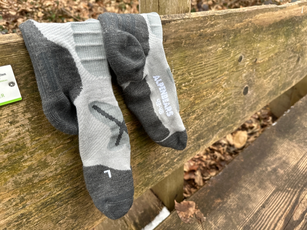 Ein Paar Alpen Bears Premium Wandersocken liegt nach dem Gebrauch auf einer Holzbank im Wald. Die Struktur der Socken ist deutlich sichtbar.