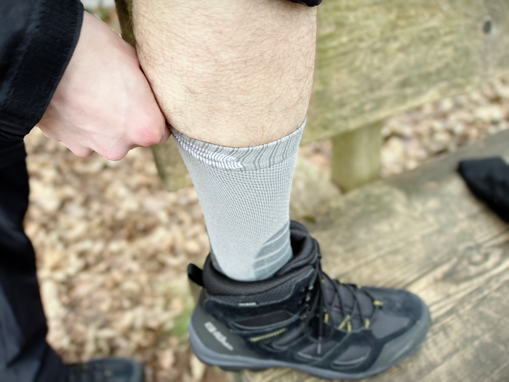 Eine Person zieht die Alpen Bears Premium Wandersocken hoch, um den Stretch-Effekt zu demonstrieren. Der Socken passt sich eng an die Wade an.