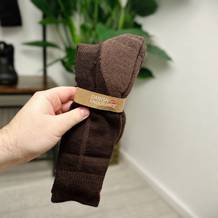 Eine Hand hält die Danish Endurance Merino Wandersocken, die mit einer Kartonbanderole umwickelt sind. Der braune Farbton und die feine Struktur der Socken sind gut sichtbar.