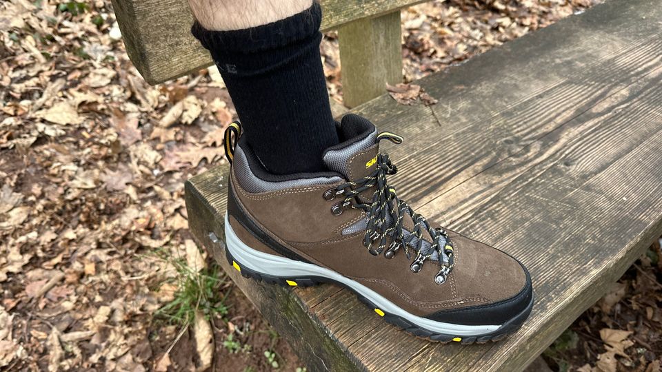 Ein Wanderer trägt die Falke TK2 Wandersocken in einem festen Wanderschuh. Das Bild wurde auf einer Holzbank im Wald aufgenommen.