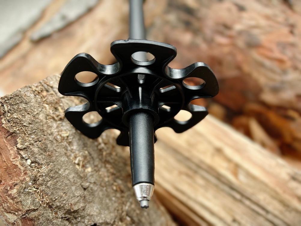 Die Spitze eines Alpen Bears Wanderstocks mit montiertem Winterteller liegt auf Holz. Der Teller hat große Öffnungen zur Schneeaufnahme.