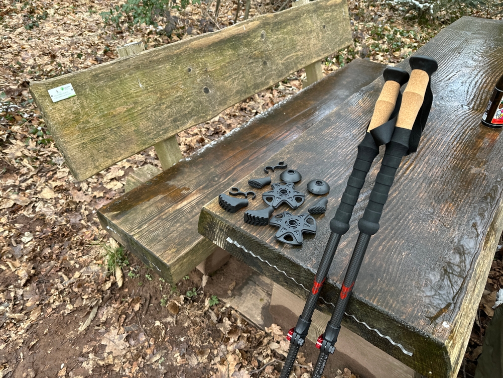 Die Rothwild Teleskopstöcke liegen mit umfangreichem Zubehör wie Gummipuffern und Tellern auf einer Holzbank im Wald.