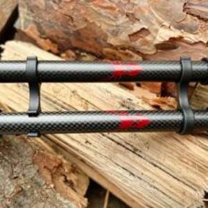 Zwei zusammengeklappte Rothwild Teleskopstöcke aus Carbon auf einer Holzbank im Wald. Die roten Logos und Carbonstruktur sind gut sichtbar.