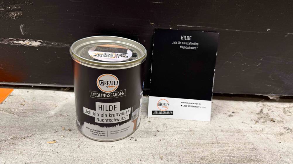 Neben der Dose Wandfarbe Schwarz steht eine Farbkarte auf dem Boden.