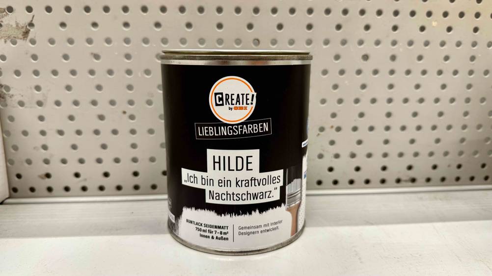 Eine Dose der getesteten Wandfarbe Schwarz auf einem hellen Regalbrett.