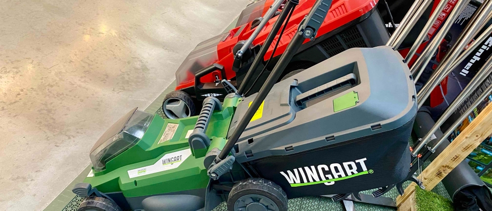 Seitliche Ansicht eines grünen Wingart-Akku-Rasenmähers im Test, der neben anderen Rasenmähern in einem Verkaufsbereich steht.