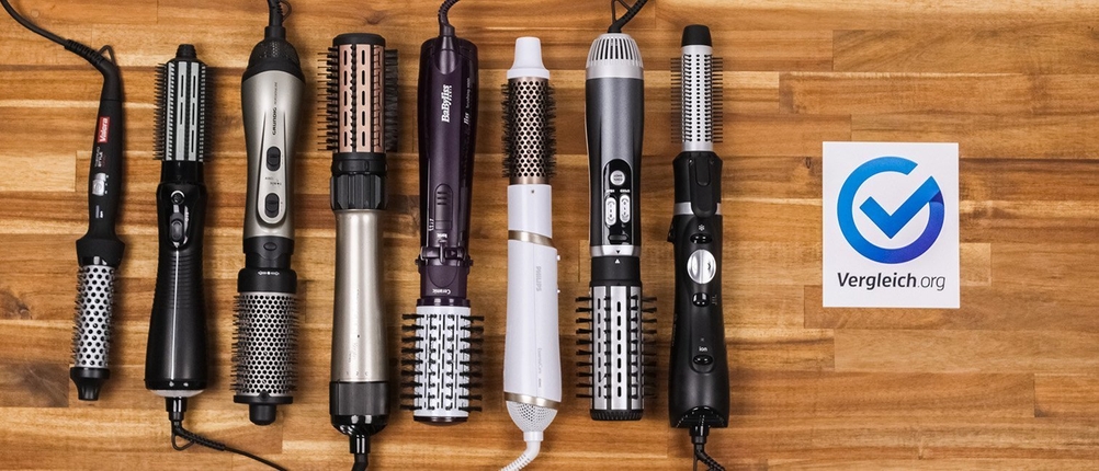Warmluftbürste-Test: Mehrere Warmluftbürsten liegen nebeneinander auf einer Holzplatte.