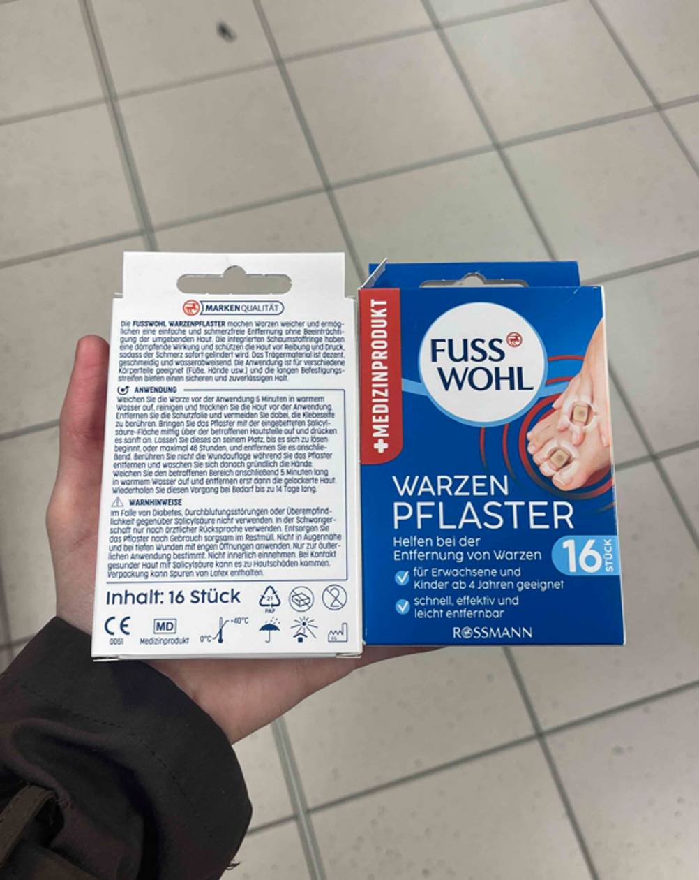 Eine Hand hält zwei Packungen der getesteten Warzenpflaster nebeneinander, einmal die Vorderseite, einmal die Rückseite.