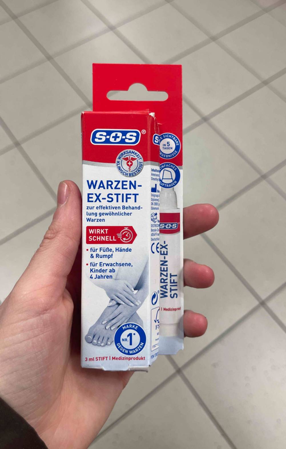 Der getestete Warzenstift der Marke SOS befindet sich innerhalb der rot-weißen Verpackung in einer Hand.