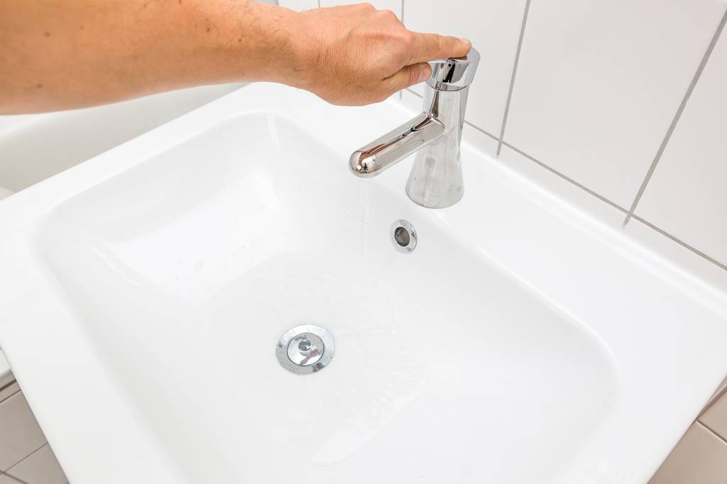 Waschbeckenstöpsel im Test: Ein weißes Waschbecken mit geschlossenem Stöpsel bei dem eine männliche Hand gerade den Wasserhahn hält.
