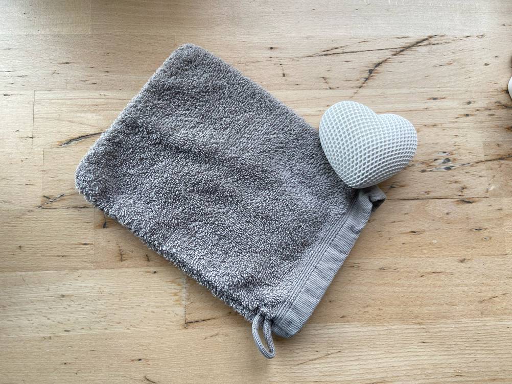 Auf einer Holzfläche liegt der getestete Waschhandschuh mit einem Dekoherz.