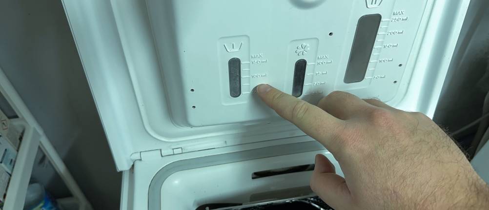 Ein Finger zeigt auf die Füllhöhe des Waschmittels für schwarze Wäsche in der Waschmaschine.