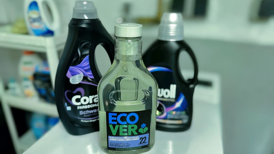 Waschmittel für schwarze Wäsche von Coral, Perwoll und Ecover stehen auf einer Waschmaschine.