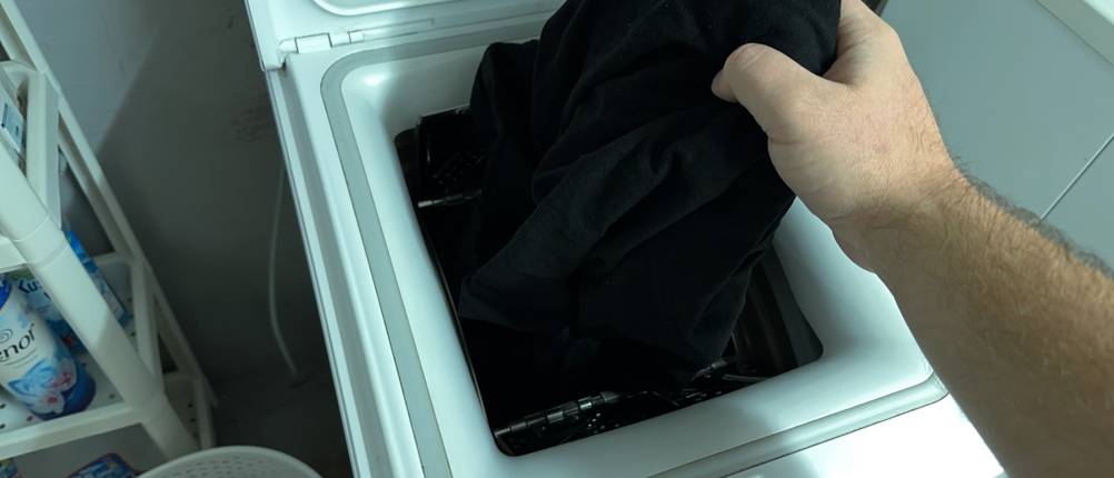 Schwarze Wäsche wird aus einer Waschmaschine entnommen.