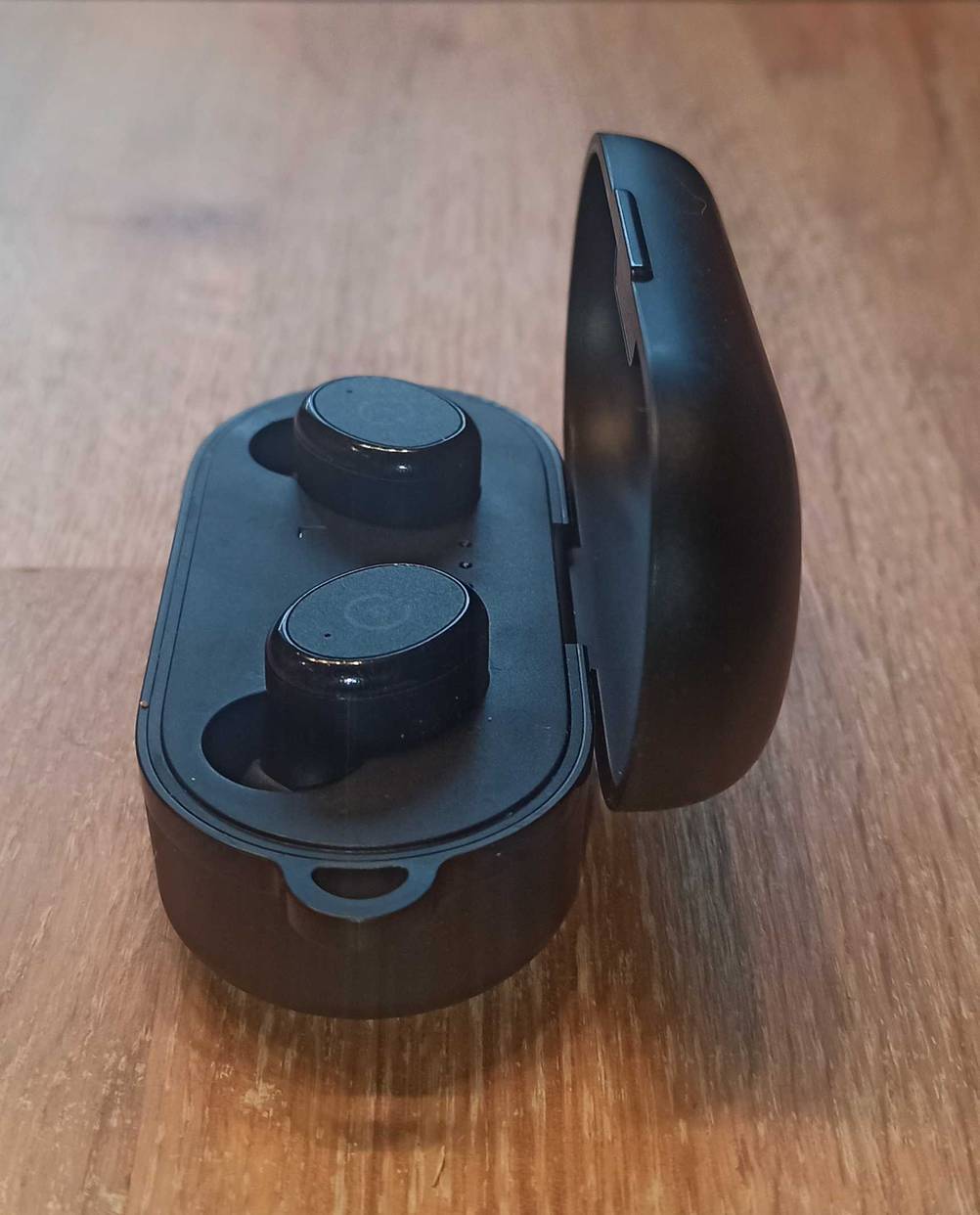 Wasserdichte Köpfhörer getestet: Die Kopfhörer in ihrem Case von der Seite auf einem Holztisch.