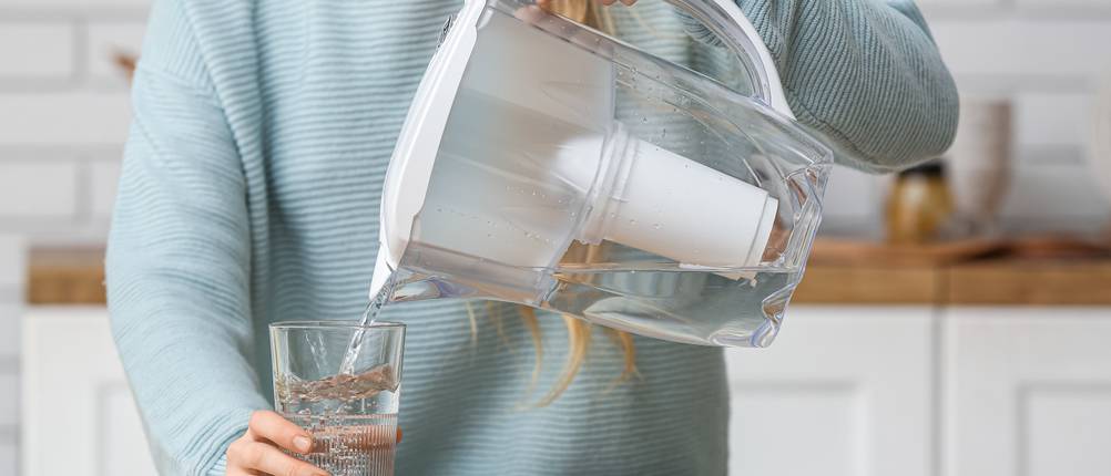 Wasserfilter im Test: Frau gießt Wasser aus Kannenfilter in Glas.