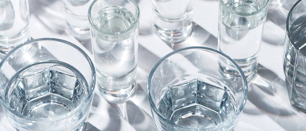 Verschiedene Wassergläser stehen teilweise gefüllt auf einem weißen Untergrund.