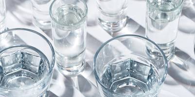 Verschiedene Wassergläser stehen teilweise gefüllt auf einem weißen Untergrund.