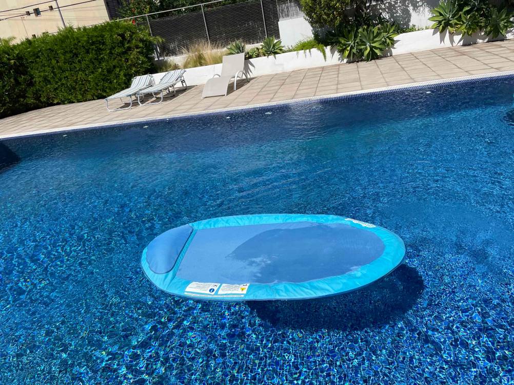 Türkisblaue, getestete Wasserhängematte schwimmt im Wasser eines Schwimmbeckens unter freiem Himmel.