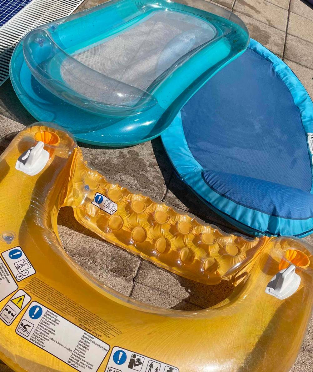 Türkisblaue Wasserhängematte im Test befindet neben weiteren transparenter und gelber Schwimmmatratze auf einer Pool-Umrandung im Freien.