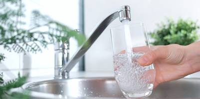 Ein Wasserglas wird unter einen laufenden Wasserhahn gehalten.