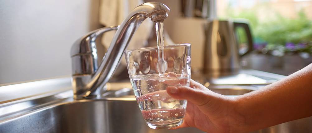Ein Glas wird unter einen laufenden Wasserhahn gehalten.