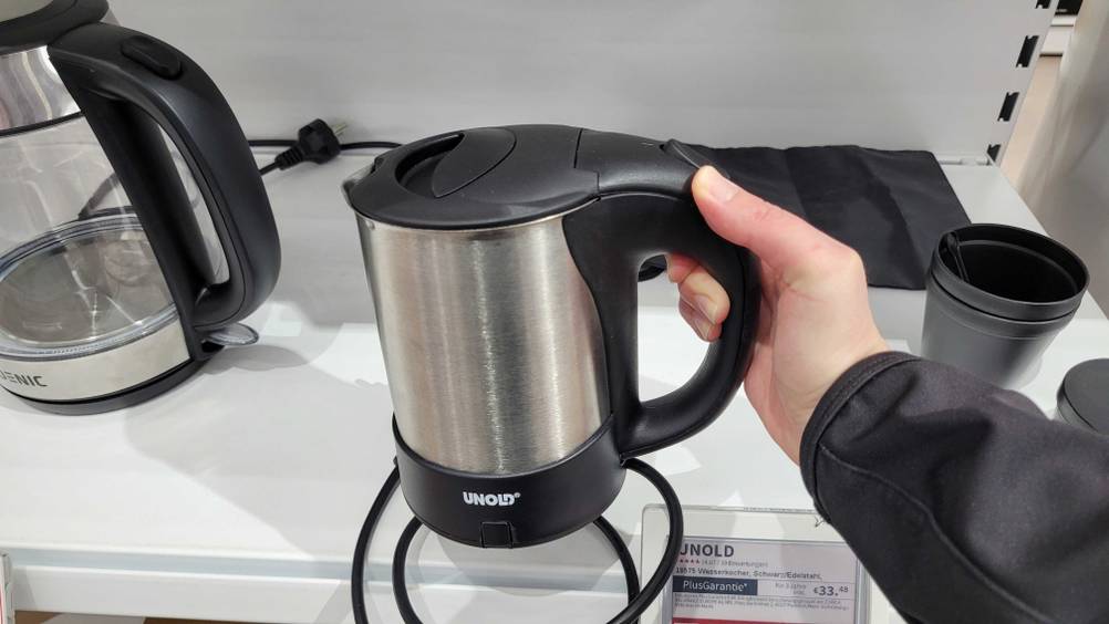 Eine Hand hält den getesteten Wasserkocher 0,5 Liter vor ein Regal.