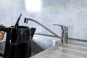 Ein Wasserkocher wird an einem Wasserhahn aufgefüllt.